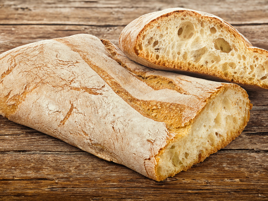 Loaf of ciabatta bread with a slice cut off on a wooden surface
