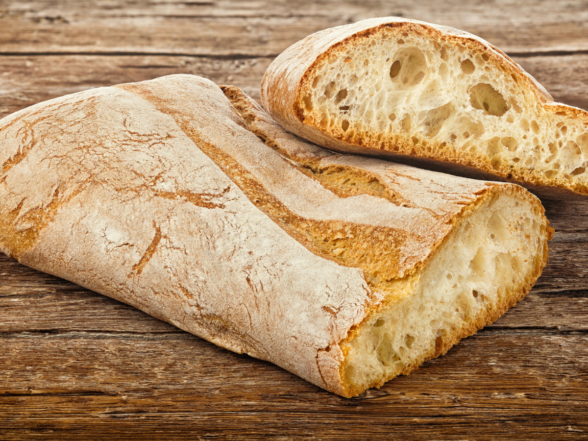 Loaf of ciabatta bread with a slice cut off on a wooden surface