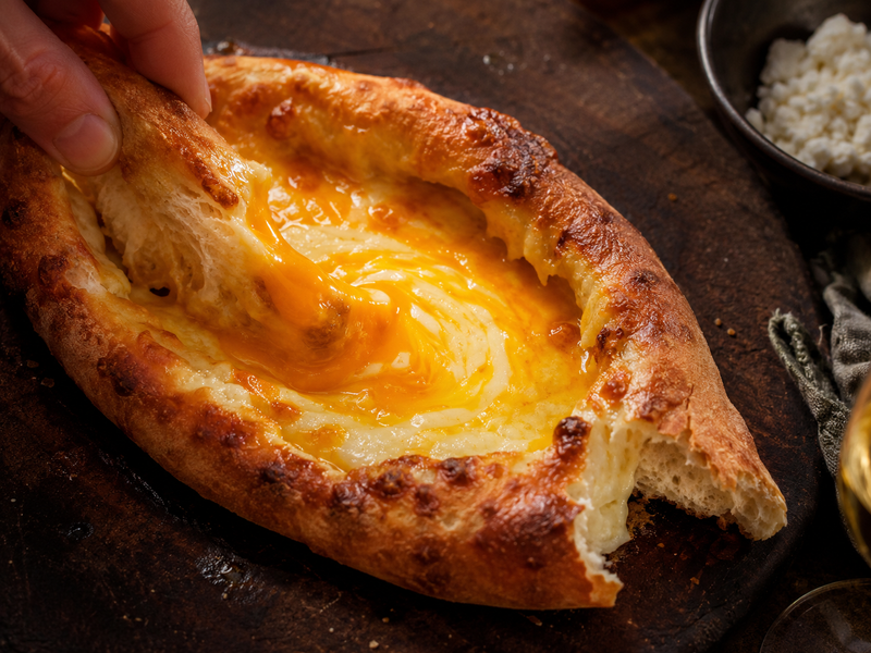 Georgian cheese boat khachapuri with egg yolk being whipped into the molten cheese with torn bread.