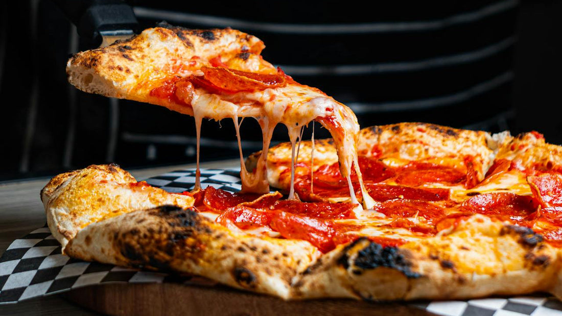 Slice of pepperoni pizza being lifted from a whole pizza on a wooden board.