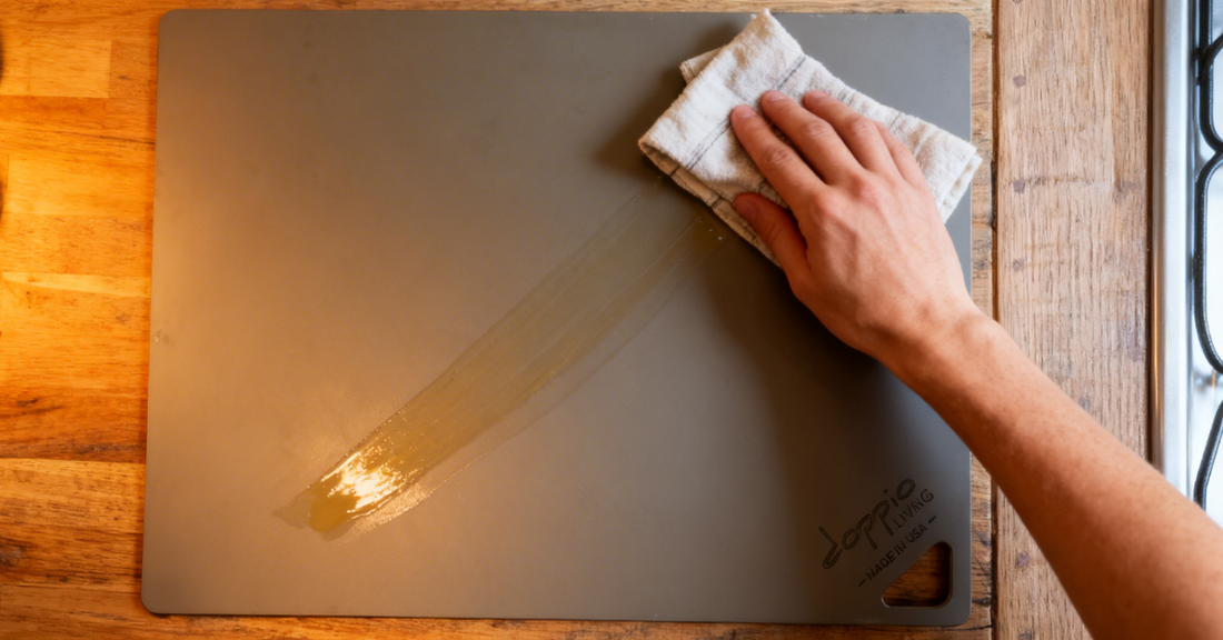 A thin layer of flaxseed oil being wiped across a carbon steel pizza steel with a folded cotton cloth