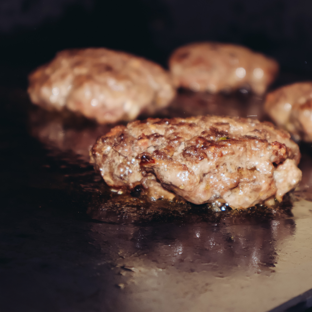 Burger patties cooking on a carbon steel pizza steel used on a grill for flat top style searing